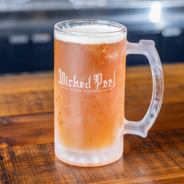 A frosty mug of beer with the "Wicked Peel Pizza Kitchen" logo on a wooden table.
