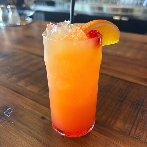 A vibrant orange and red cocktail with ice, an orange slice, and a cherry on a wooden table.
