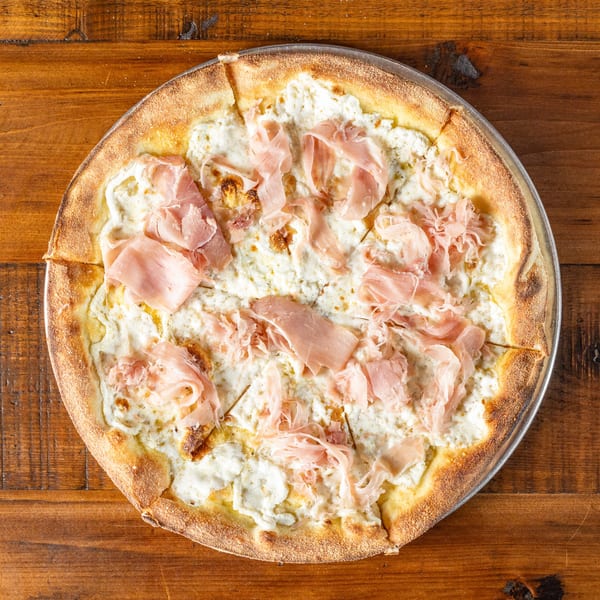 Wicked Peel Pizza's white pizza with ricotta cheese and thinly sliced prosciutto on a wooden table.