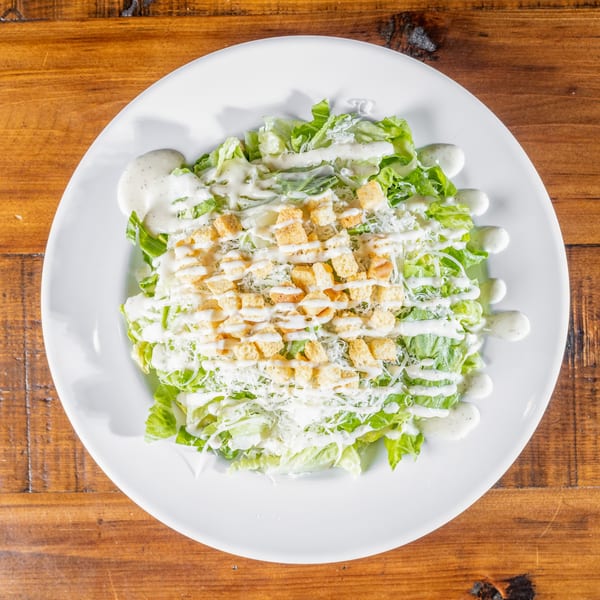 A Caesar salad with lettuce, croutons, shredded cheese, and dressing on a white plate.