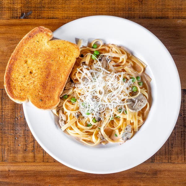 Creamy fettuccine pasta with mushrooms, peas, and grated cheese, served with garlic bread.