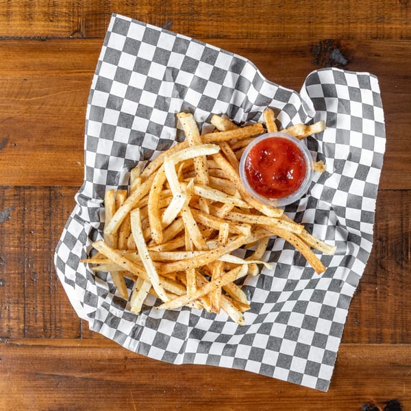 A basket of golden-brown french fries with a side of ketchup on a checkered paper liner.