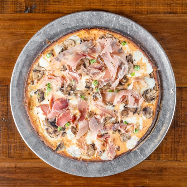 Wicked Peel Pizza with prosciutto, mushrooms, and white sauce on a metal pan.
