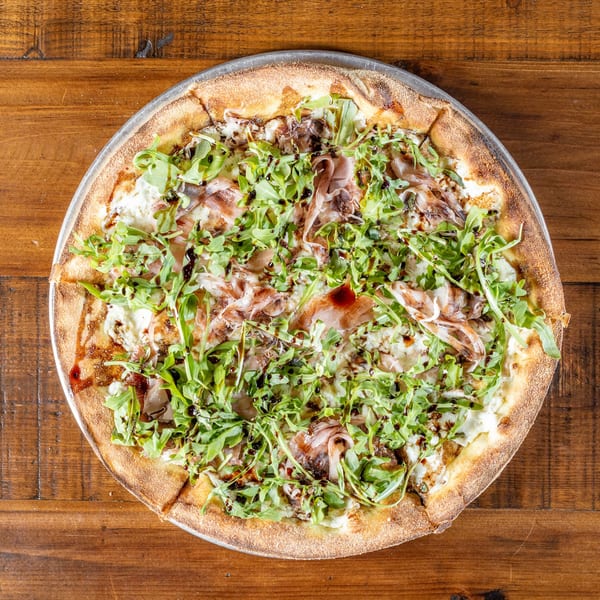 Wicked Peel Pizza's prosciutto and arugula pizza with balsamic glaze on a wooden table.